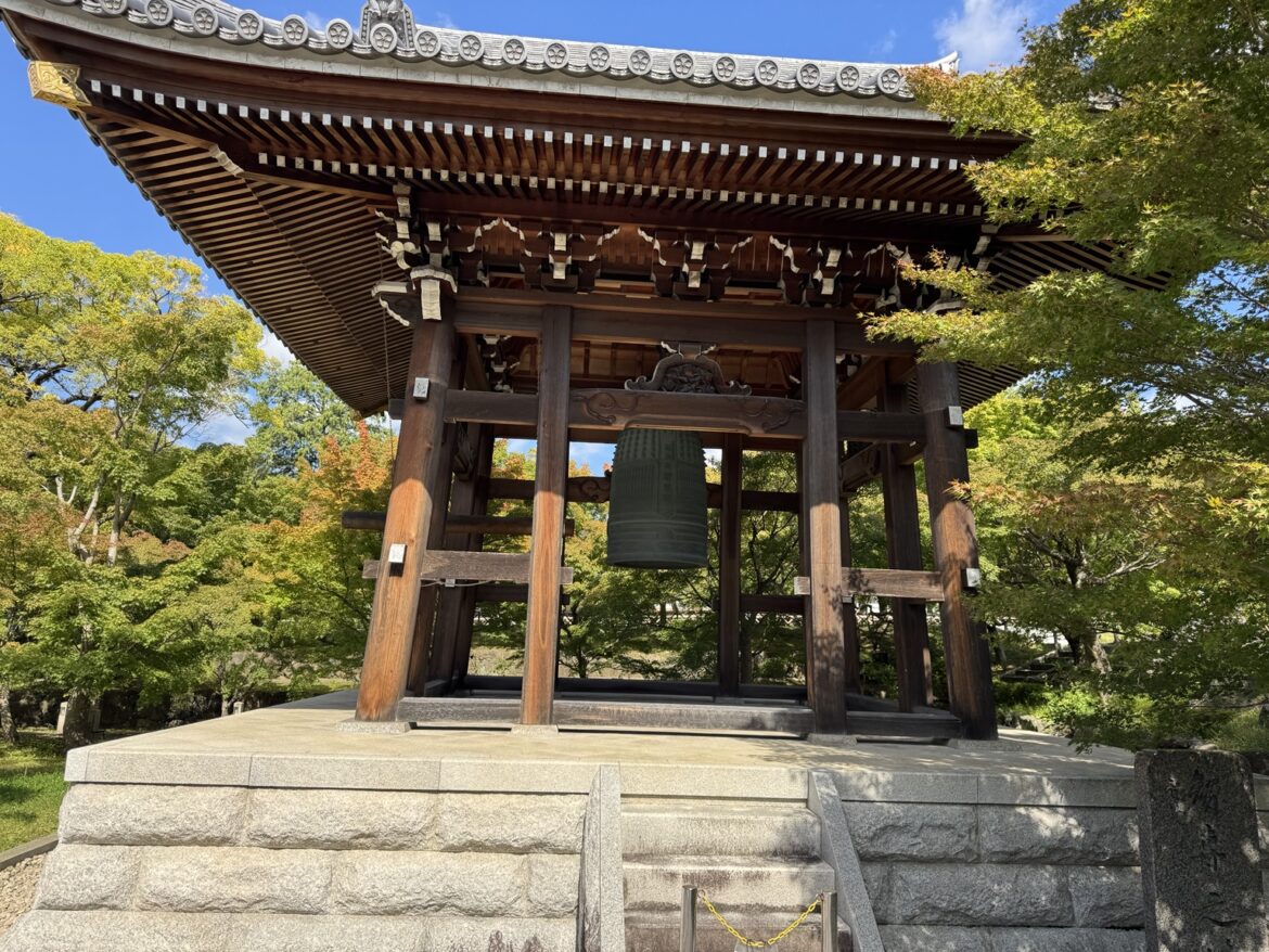 Wooden temple bell pavilion surrounded by green trees in Kyoto.